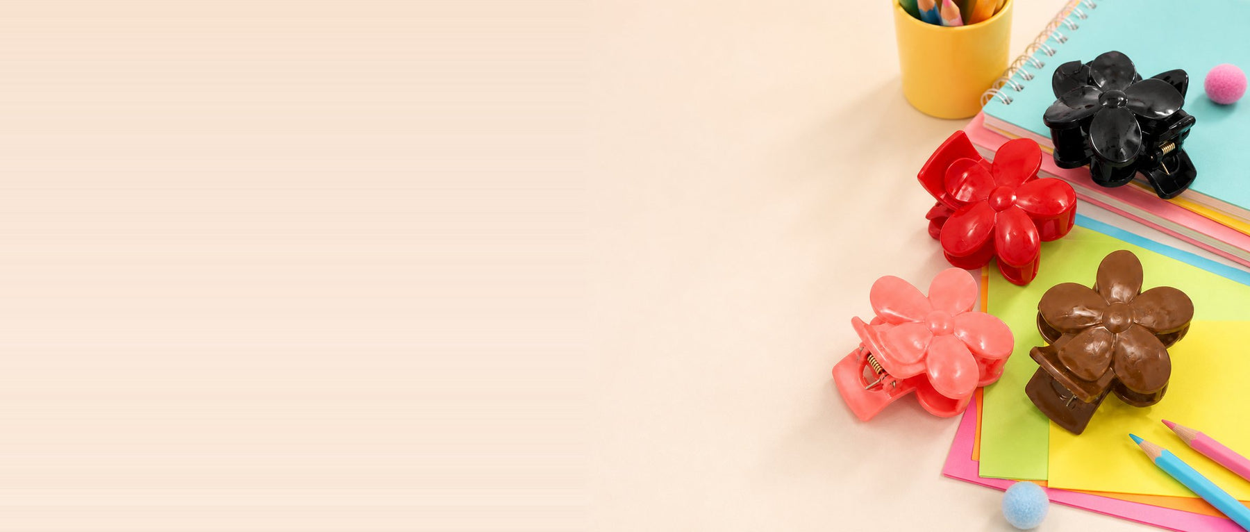 Red, black, peach and brown flower-shaped hair claw clips on coloured paper with pencils